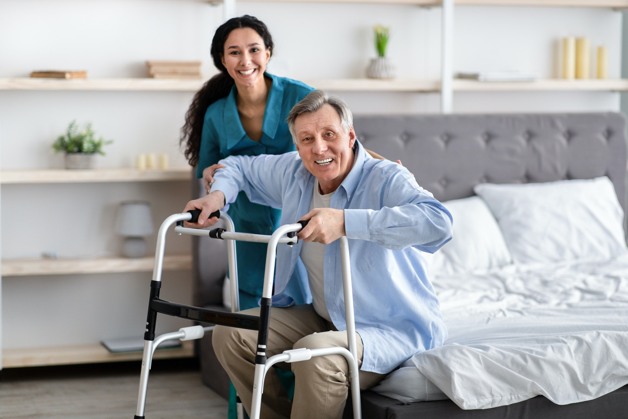 female-nurse-helping-elderly-male-with-walking-frame-stand-up-from-bed-at-home-professional-care.jpg